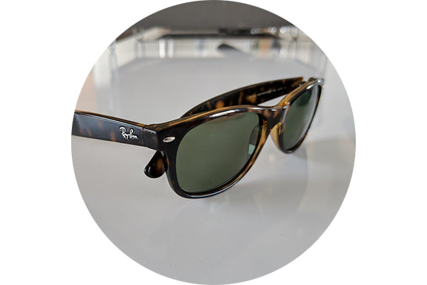 View of a pair of Ray Ban sunglasses laying on a table with Gray Green sunglass lenses installed.