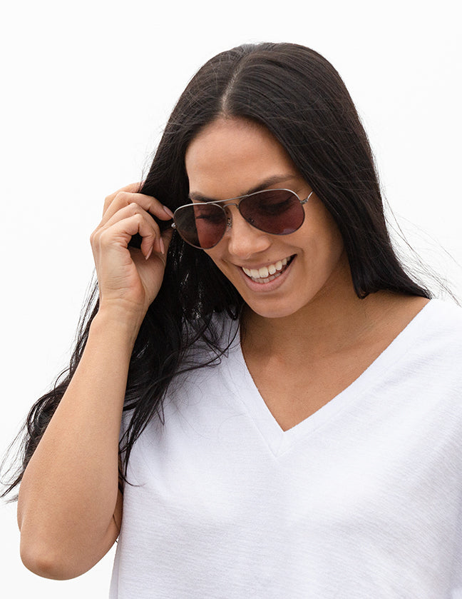 Shoulders-up view of a model with long, dark hair smiling and wearing sunglasses with Adapt orange photochromic lenses.