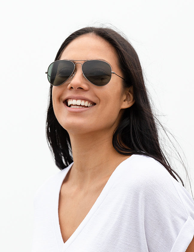 Shoulders-up view of a model with long, dark hair smiling and wearing sunglasses with Gray Green Lenses.